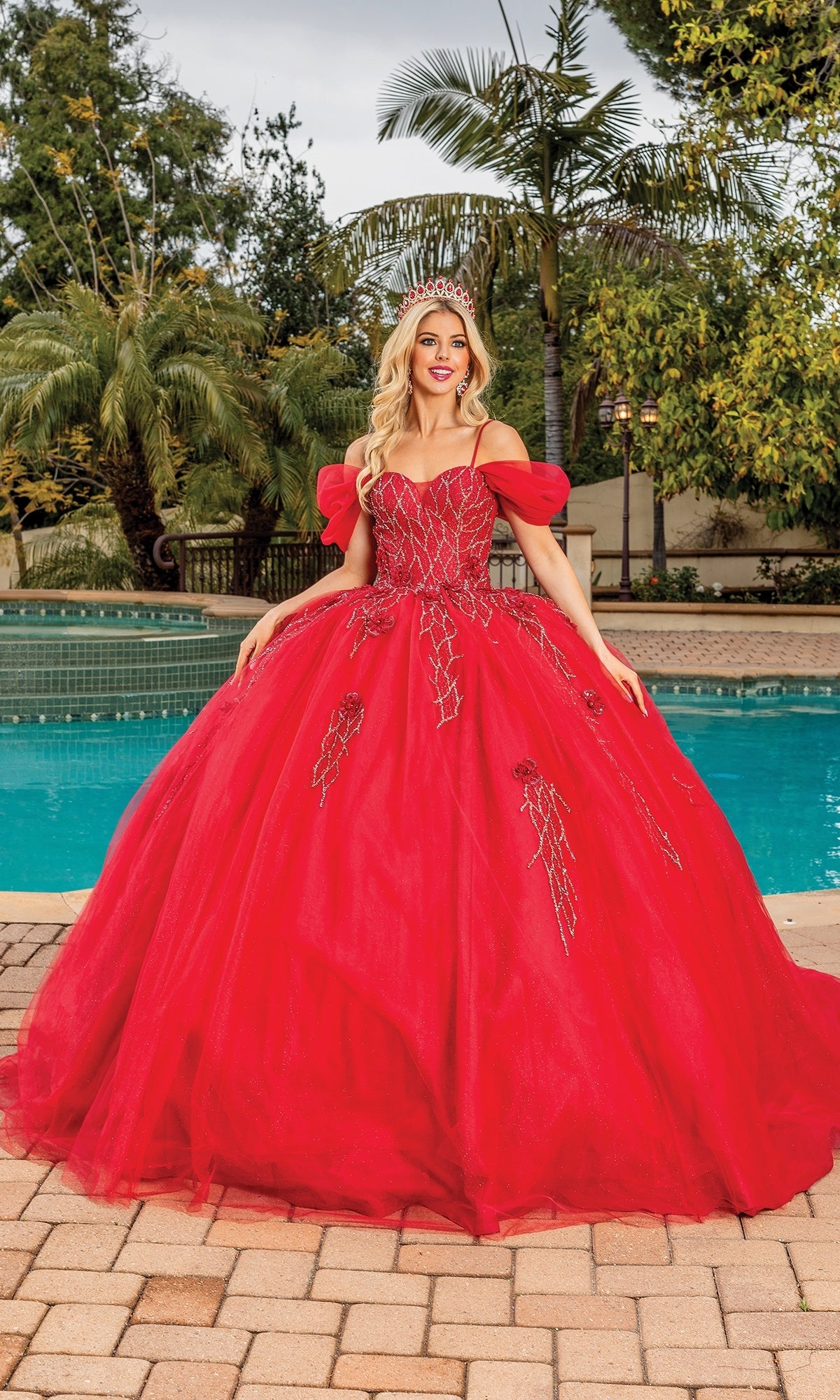 A woman in the Quinceanera Dress 1873 By Dancing Queen, featuring burgundy off-shoulder puff sleeves and beaded details, stands by a swimming pool wearing a tiara and smiling.